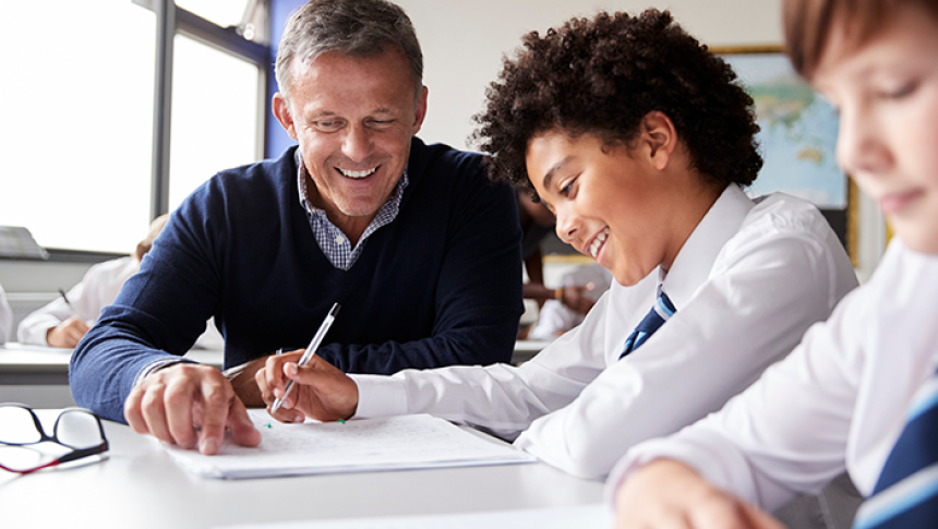 High School Teacher Giving Male Student Wearing Uniform One To One Tuition At Desk