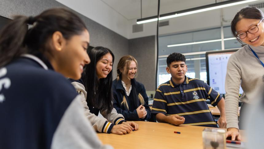 Students sit around a table with a teacher in front