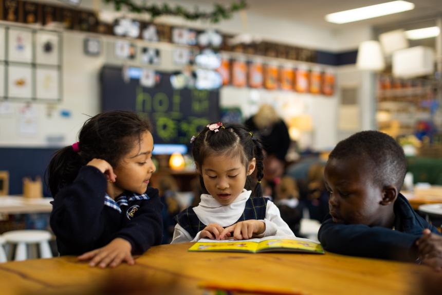 Two female students and one male student from different cultural backgrounds reading together in a classroom.